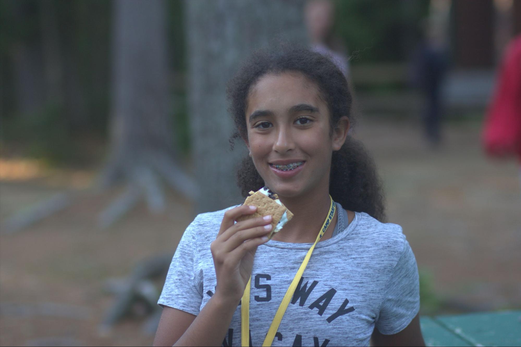 Summer camp girl holding a s’more smiling at camera at Camp Starfish