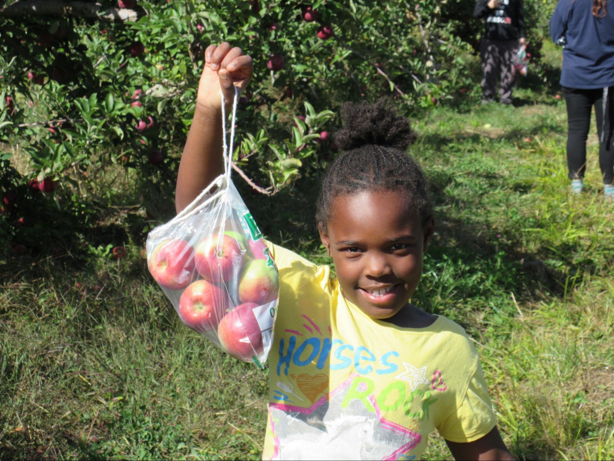 Summer camp girl smiling and holding a bag of apples she picked at Camp Starfish