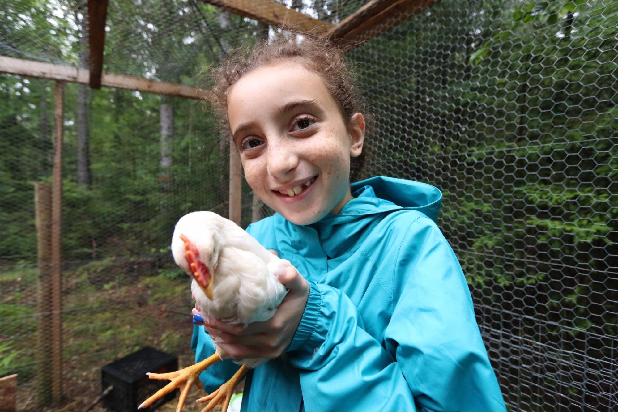 Camper girl holding chicken and smiling at the camera at Camp Starfish