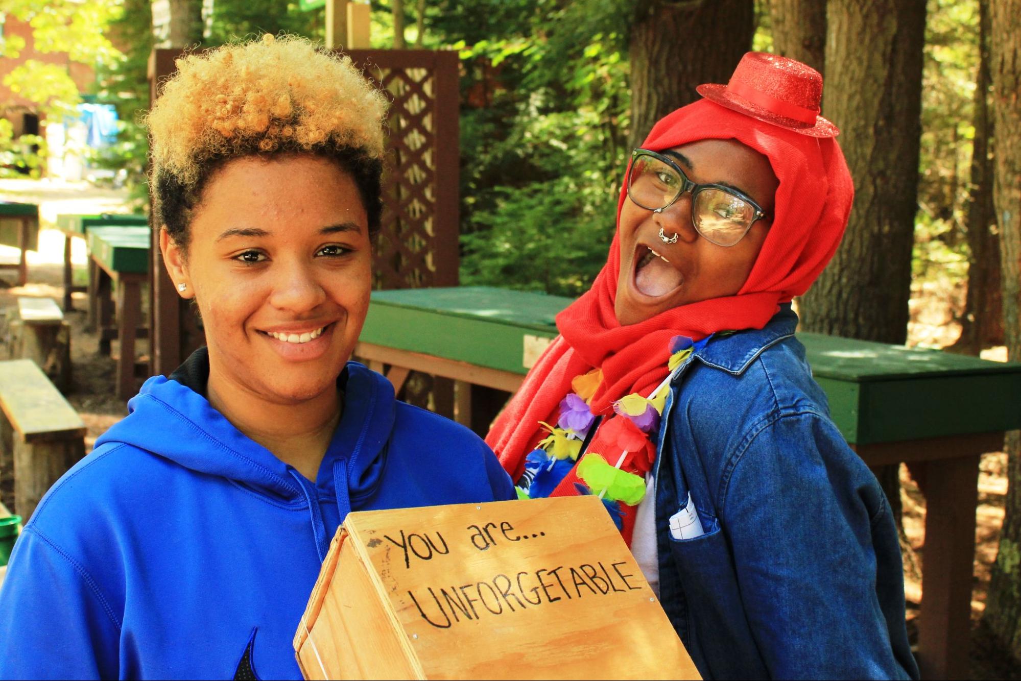 Two summer camp teens smiling at the camera holding a box that says “you are unforgettable” at Camp Starfish